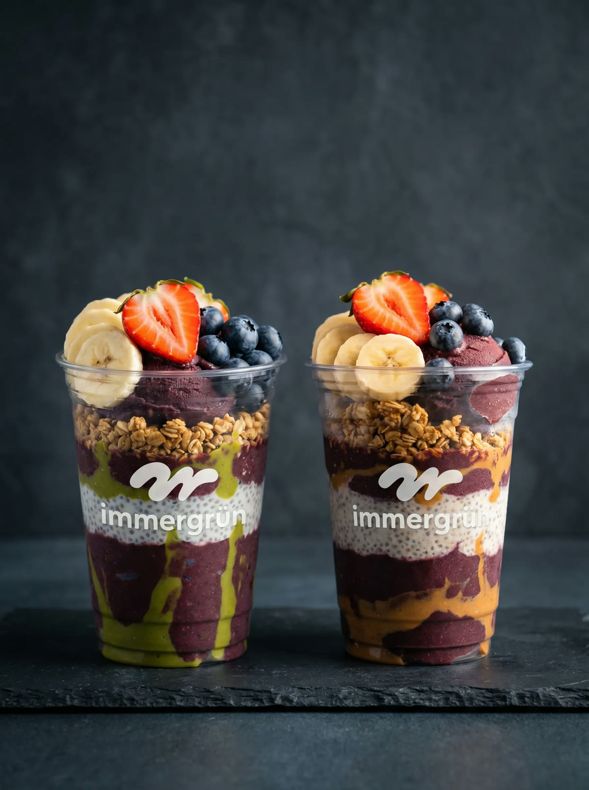 Zwei geschichtete Açaí-Becher mit frischen Beeren und Banane